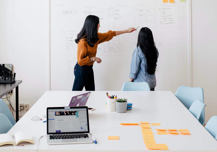 Two women collaborating on a project using a whiteboard in a modern office. Two women collaborating on a project using a whiteboard in a modern office.