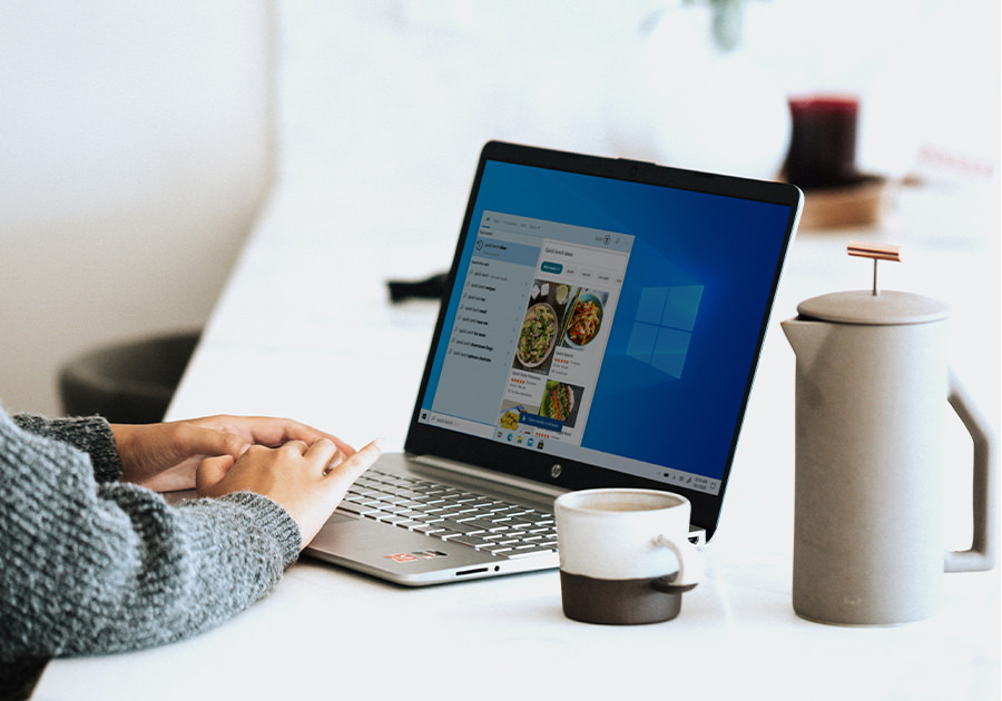 Person using a laptop with a coffee cup and French press on a white table. Person using a laptop with a coffee cup and French press on a white table.